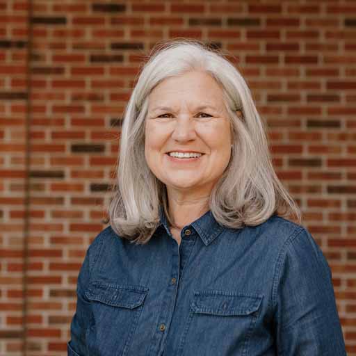 Woman with gray hair smiling in front of a brick wall