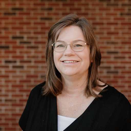 Portrait of a smiling woman with glasses in front of a brick wall