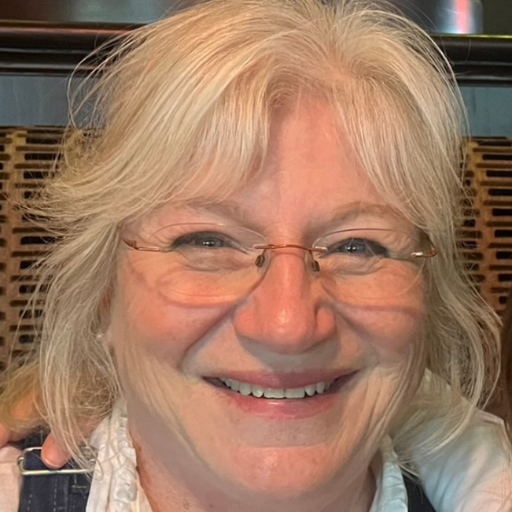 Kathy Martin, a smiling woman with blonde hair and glasses, wearing overalls.